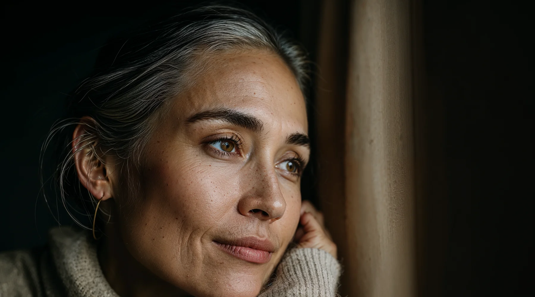 Pencere kenarında düşünceli sessiz bir an; gri saçlı kadın portresi — sağlık kararları üzerine iç tartışma teması