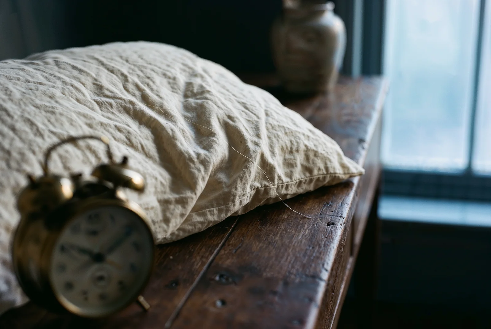 Ahşap masada krem yastık ve buğulu pirinç çalar saat, arka planda pencere.